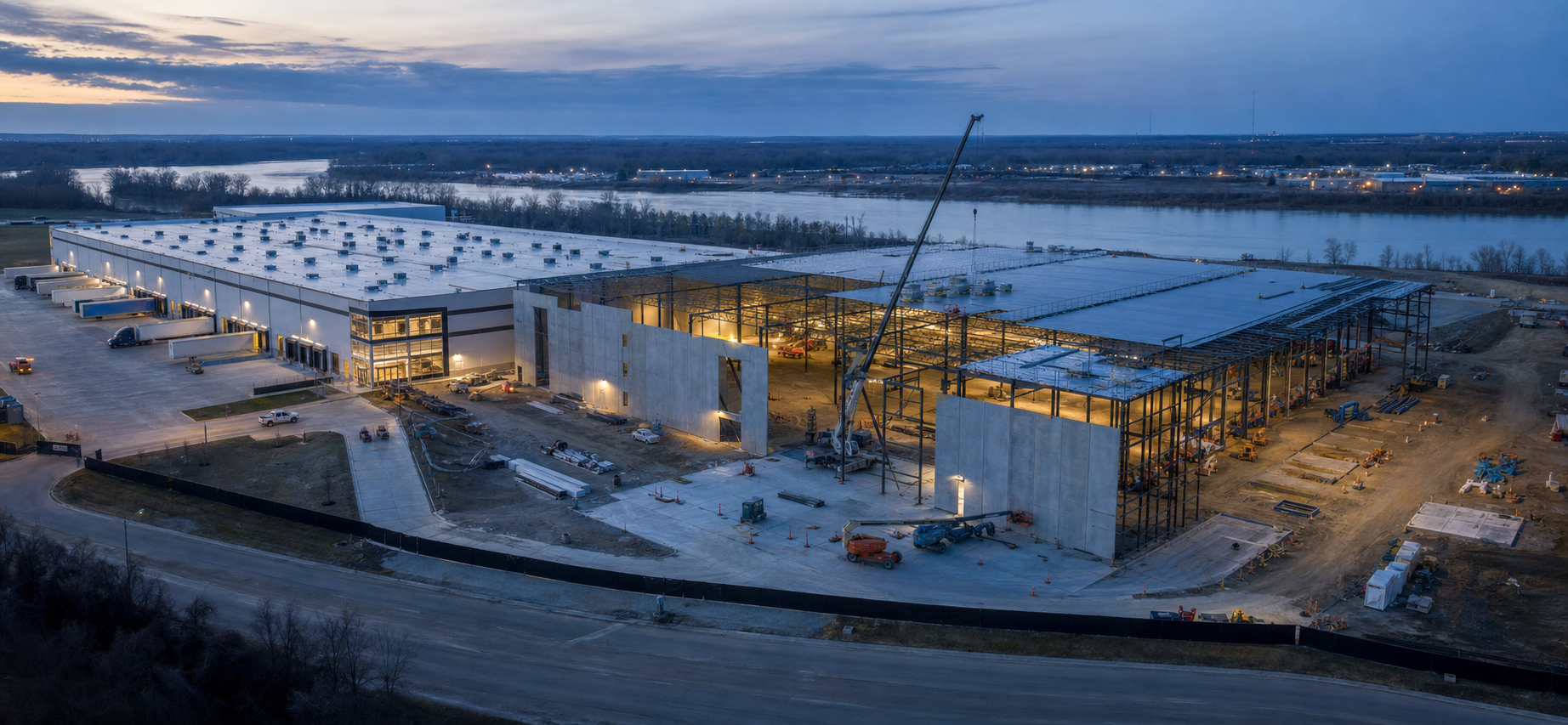 Aerial view of an occupied industrial campus expansion under construction beside a river